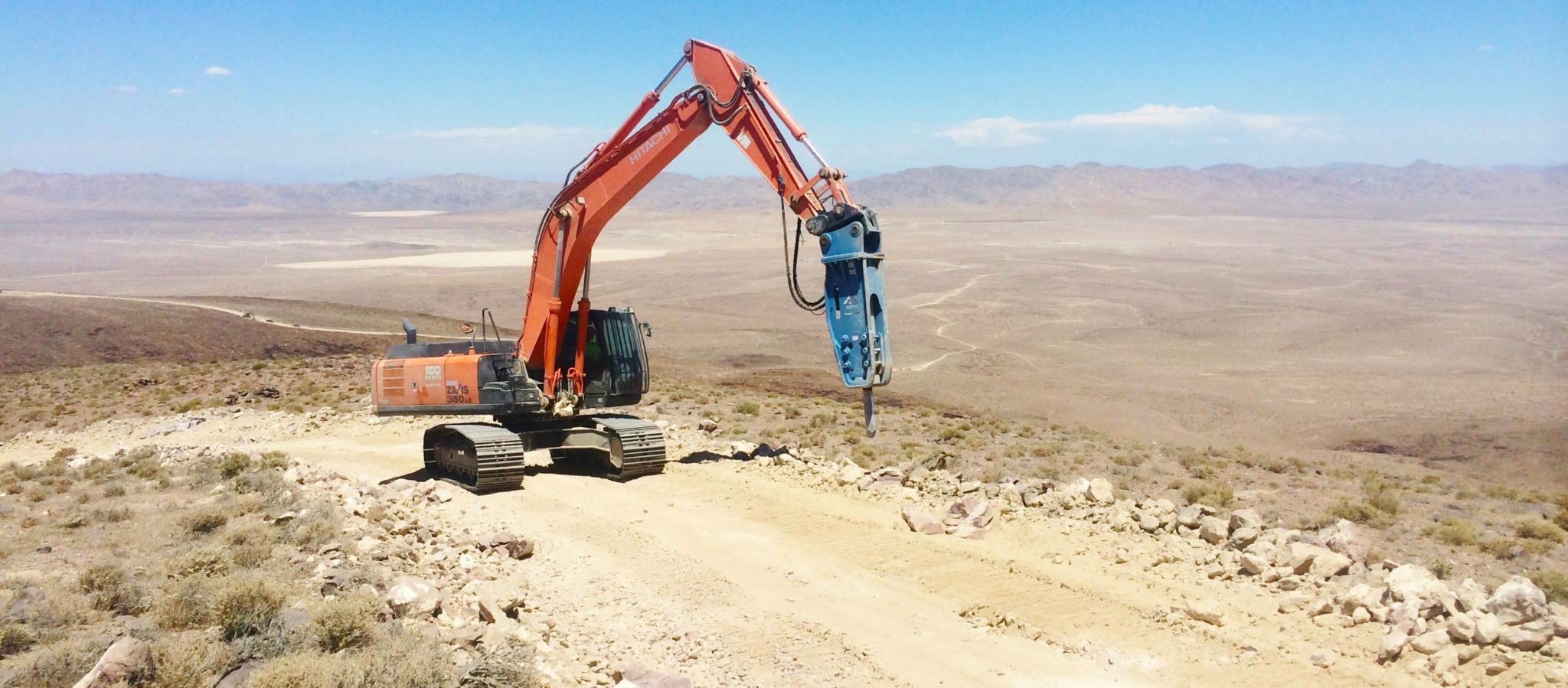 excavator with hammer attachment works to make access road in remote desert